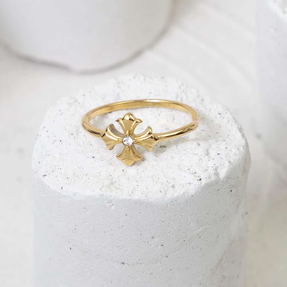 Gold ring with a cross design on a white stone surface
