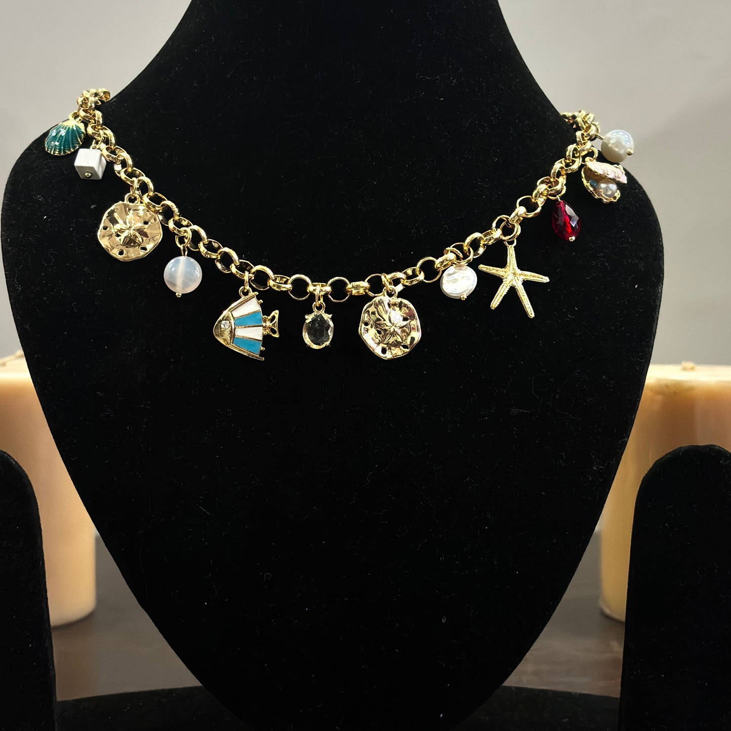 An 18K gold plated charm necklace with various charms including coins and pendants displayed on a mannequin.