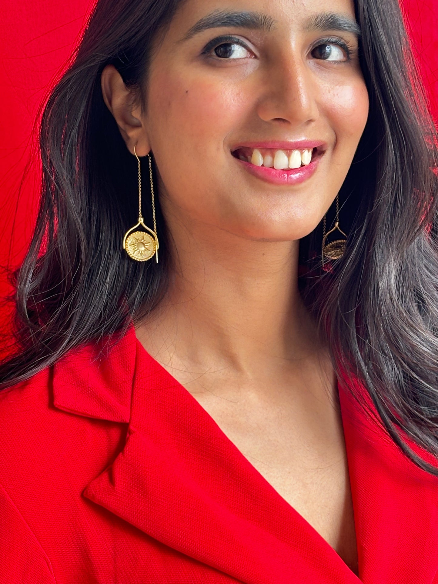 A pair of 18k gold reversible earrings, one side showing a sun design and the other side showing a moon design, displayed on a model