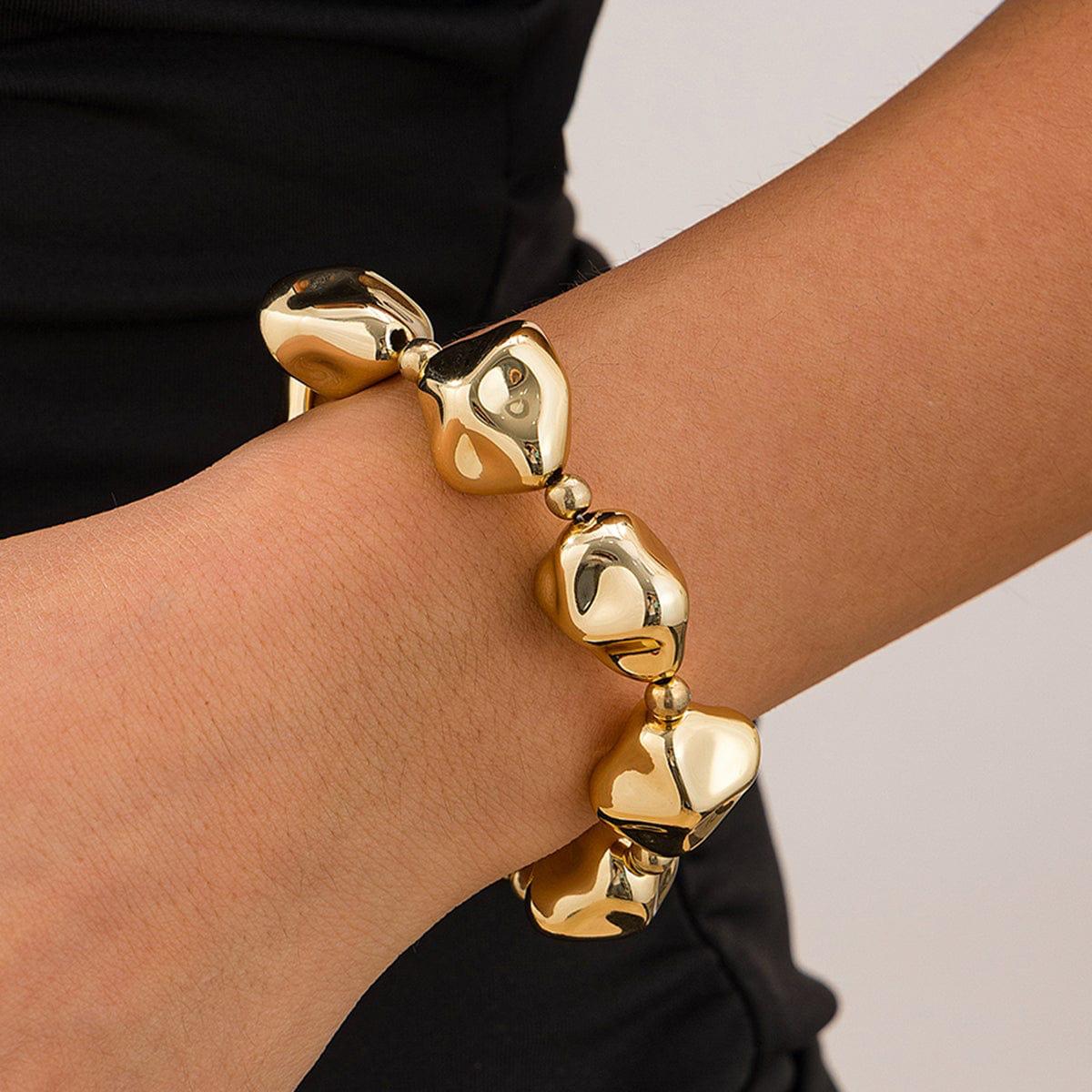 A gold-colored bracelet with pebble-shaped beads, displayed on a model hand