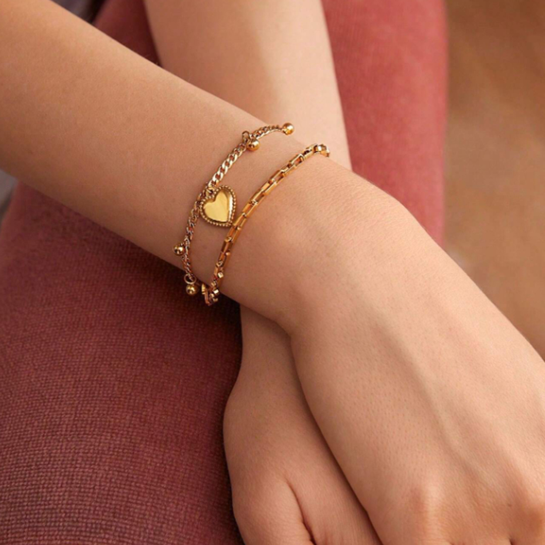 A gold-colored layered bracelet featuring heart charms and small bell-like embellishments on a hand