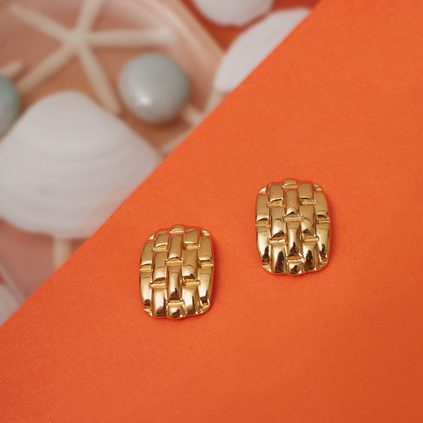 A pair of gold-plated earrings with an honeycomb design, displayed on an orange surface.