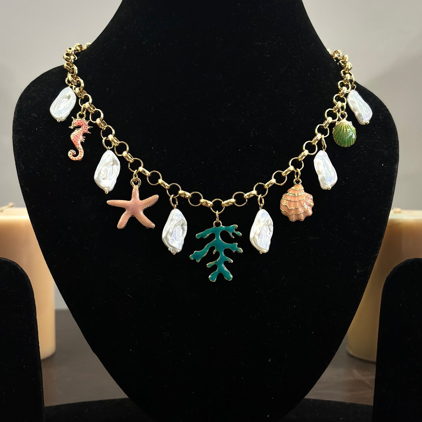 An 18K gold plated charm necklace with various charms including coins and pendants displayed on a mannequin.