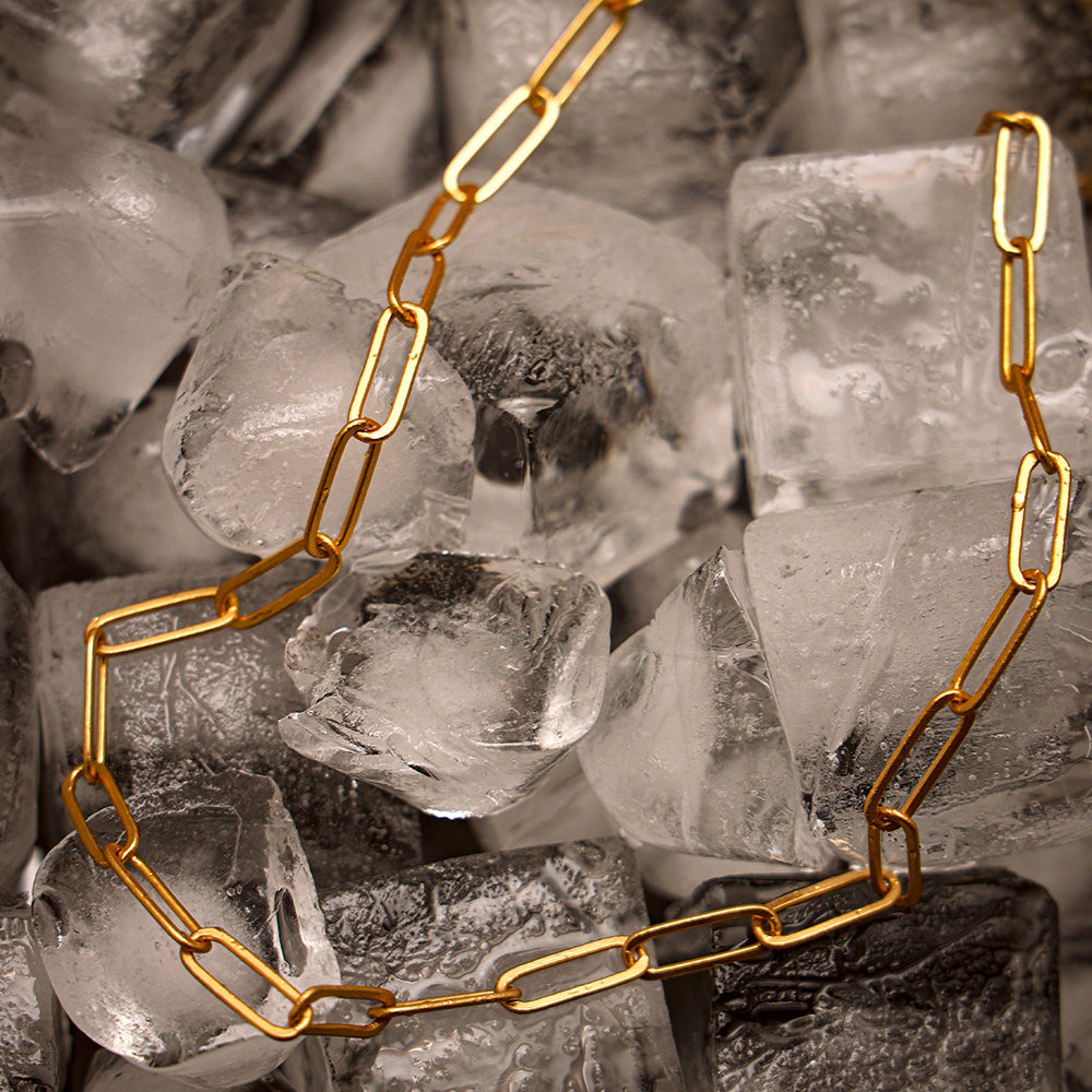 A gold-plated link chain necklace displayed on a surface with ice cubes, showcasing its sleek and minimalist design.