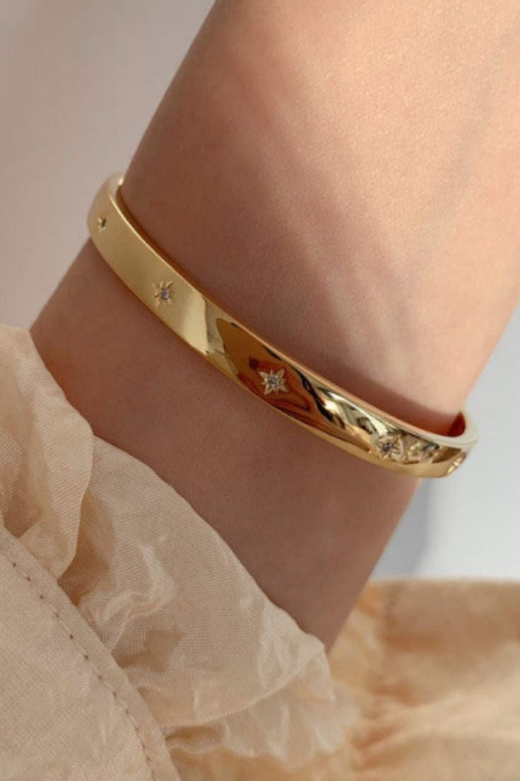 An 18k gold plated bracelet with star-shaped studs, displayed on a wrist.