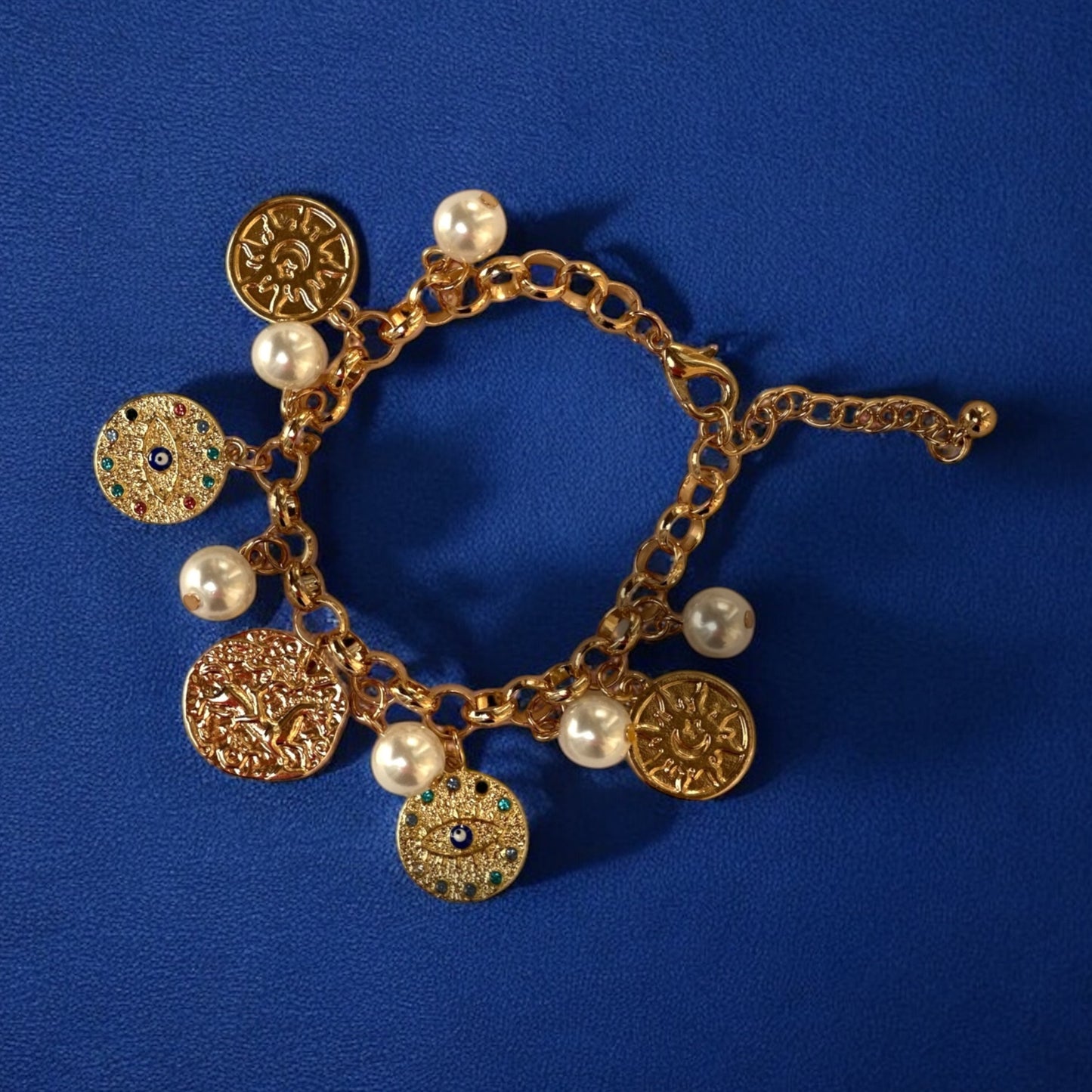 An 18K gold plated charm bracelet with a series of gold coin charms and pearl beads on a blue background.