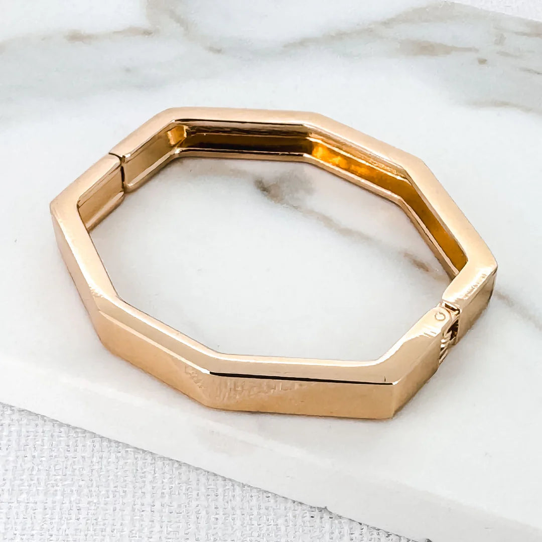A gold-plated octagon bracelet on a marble surface.