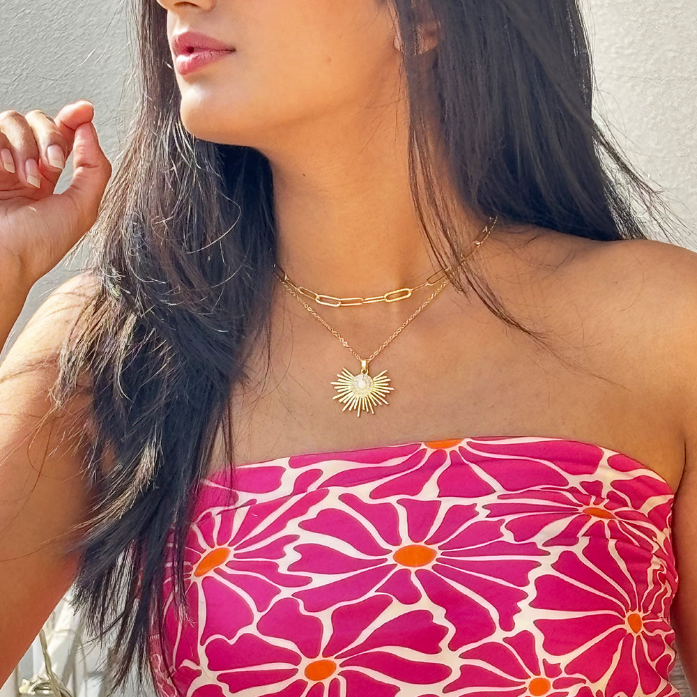A person wearing a gold-plated necklace with a half sun enamel pendant,