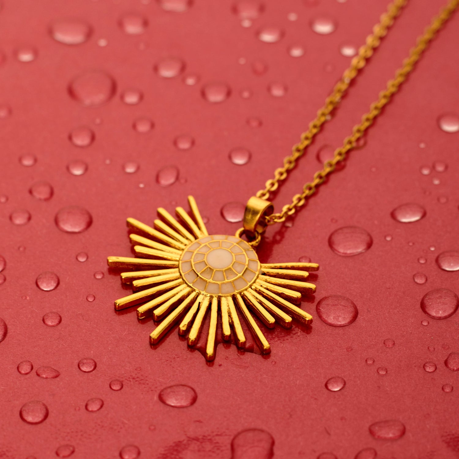 gold-plated necklace with a half sun enamel pendant, held up against a red background.