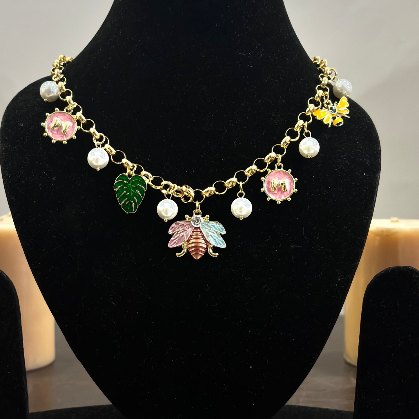An 18K gold plated charm necklace with various charms including coins and pendants displayed on a mannequin.