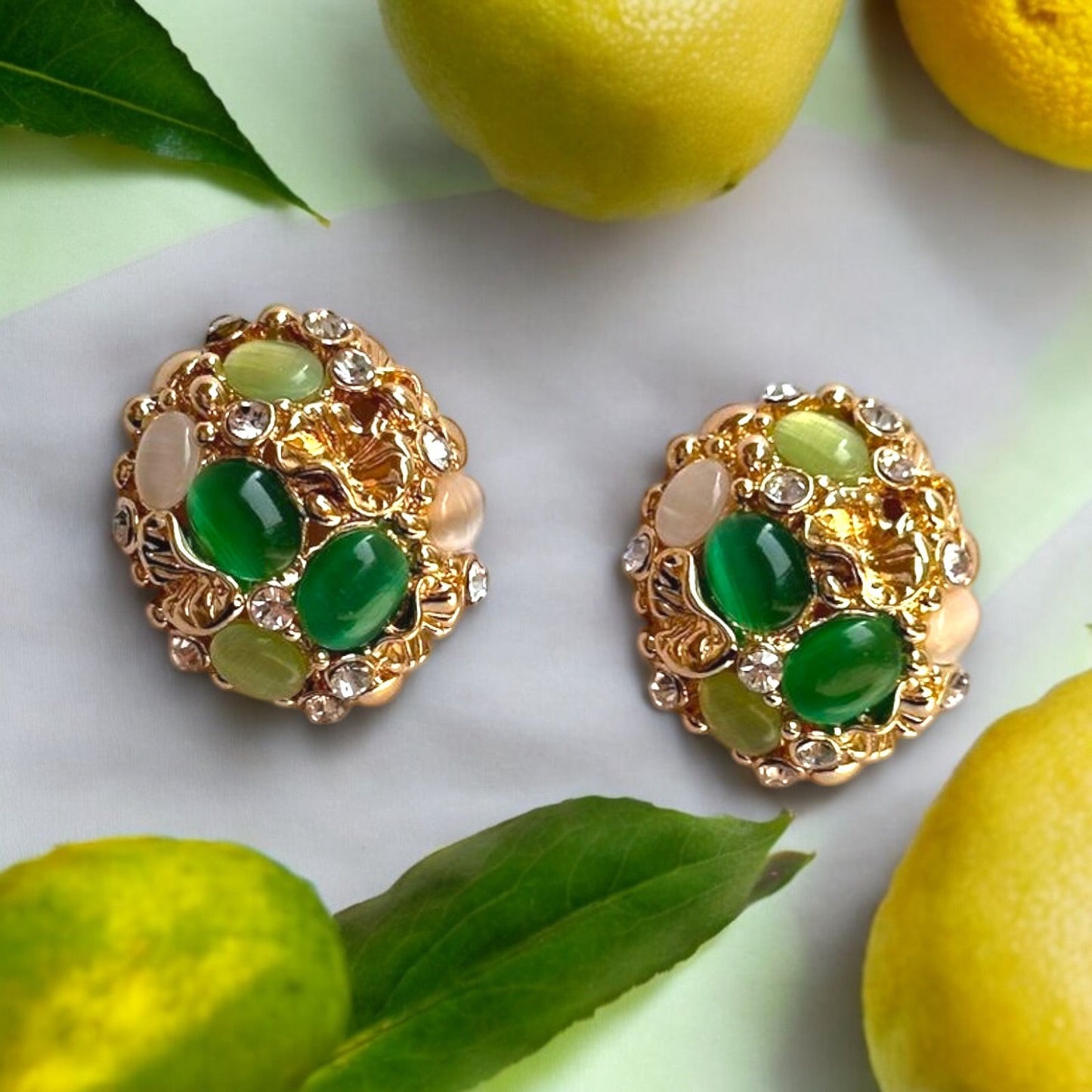 A pair of vintage-inspired green gemstone cluster earrings with gold-tone textured frames, displayed alongside citrus fruit for a pop of color.