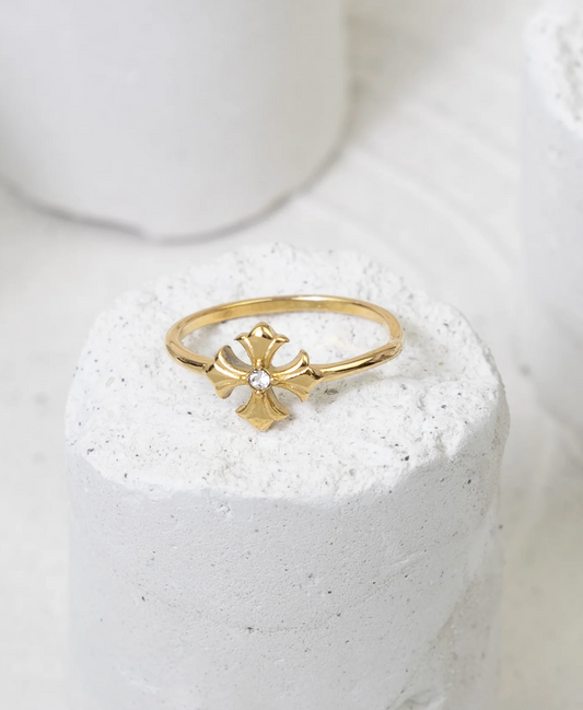 Gold ring with a cross design on a white stone surface
