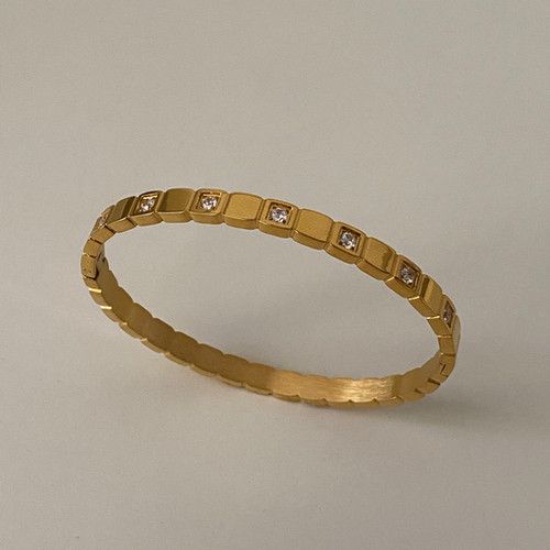 A gold-plated bracelet with a unique design that is bold at the center and tapers towards the clasp, displayed against a grey background.