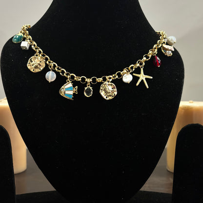 An 18K gold plated charm necklace with various charms including coins and pendants displayed on a mannequin.
