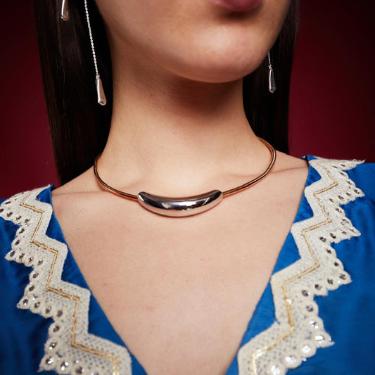 A person wearing a blue dress and a crescent-shaped pendant necklace with a gold tone and a chain strap.