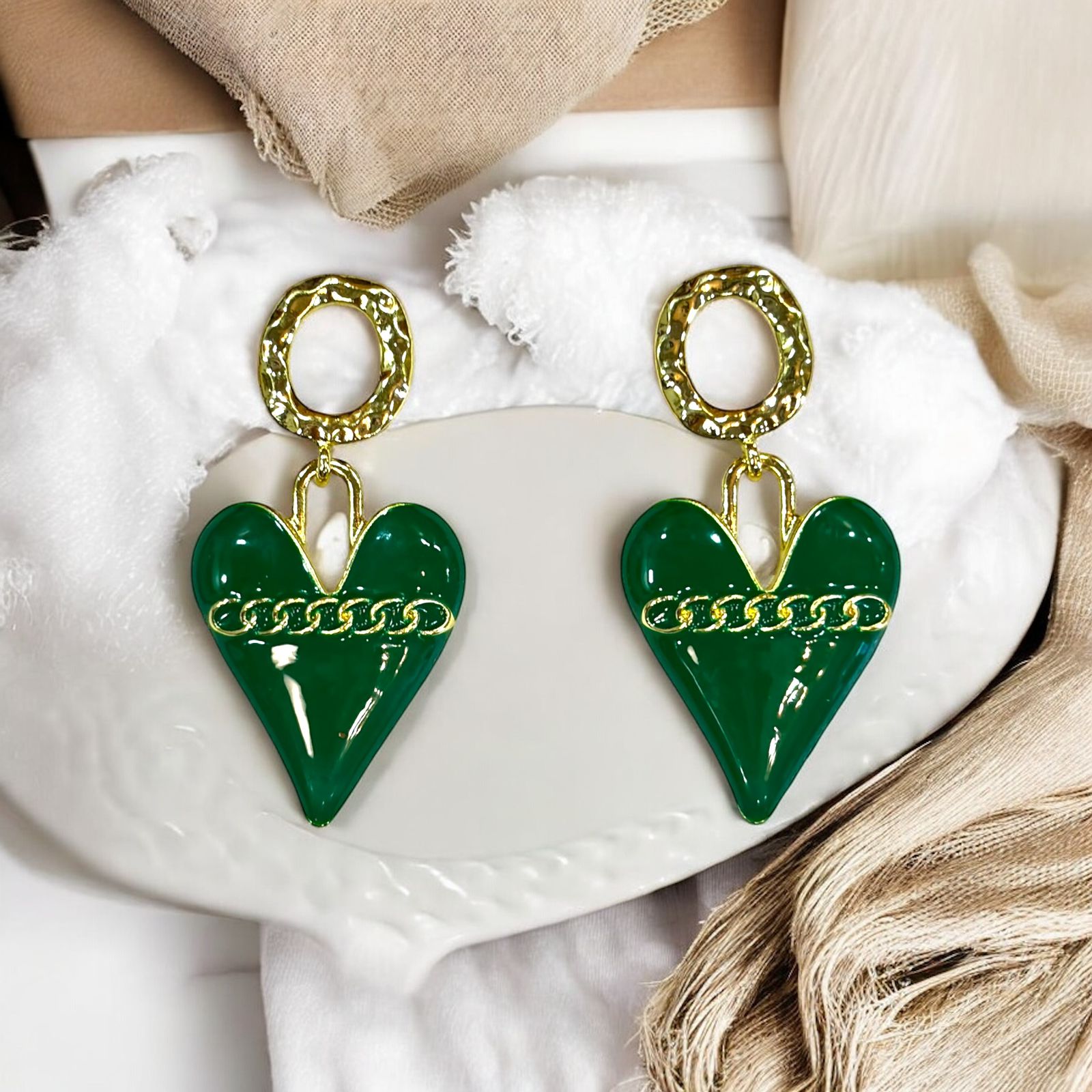 A pair of green heart-shaped drop earrings with gold chain details and gold-tone circular studs, displayed on a white surface.