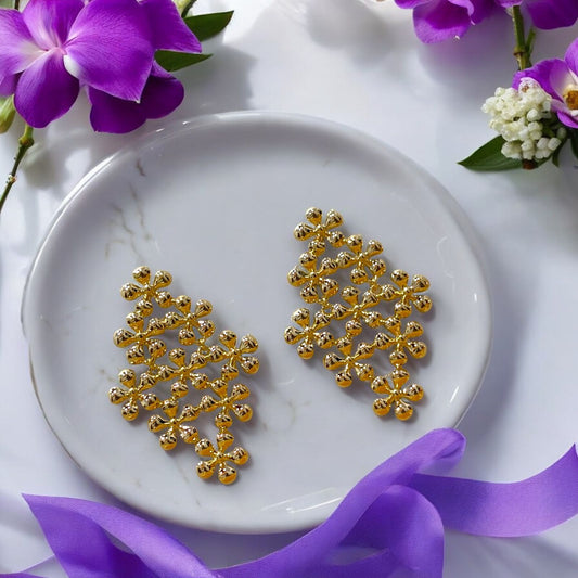 A pair of gold-colored floral-patterned dangler earrings on a white plate