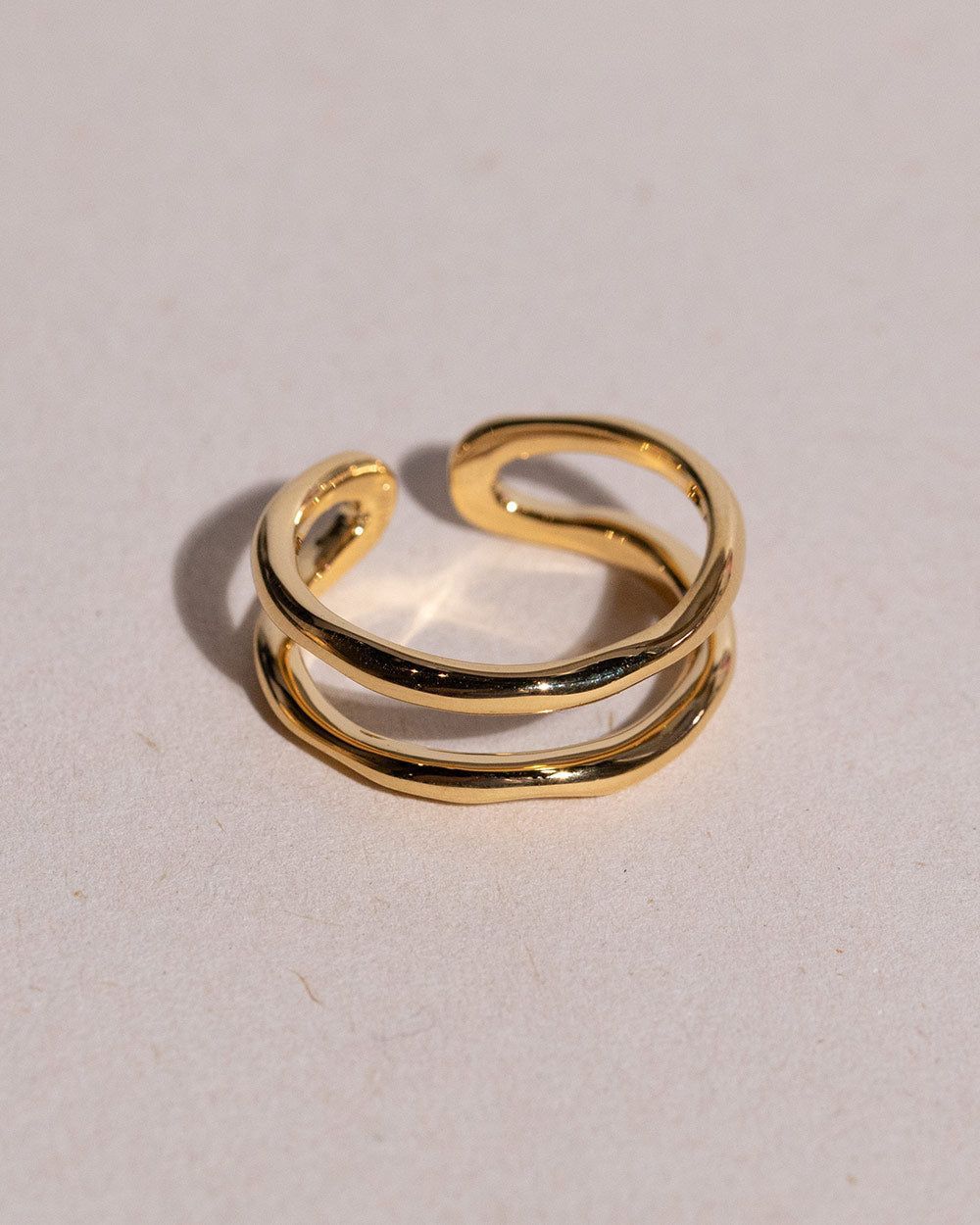 A golden spiral-shaped ring with an open band design, placed on a textured surface.