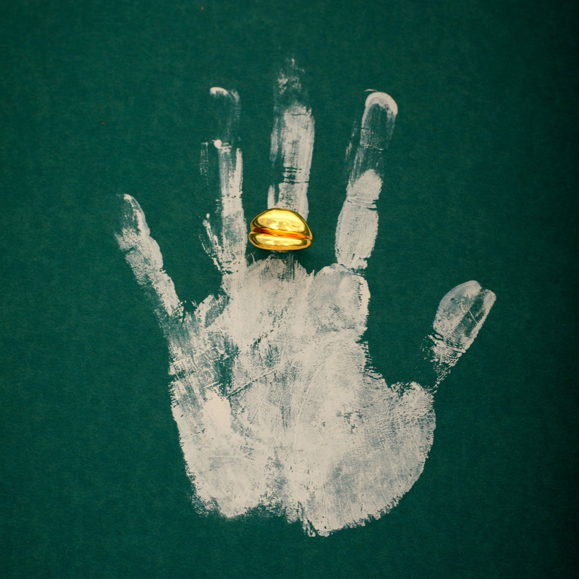 gold plated dual shaped ring in a painted hand on a green background