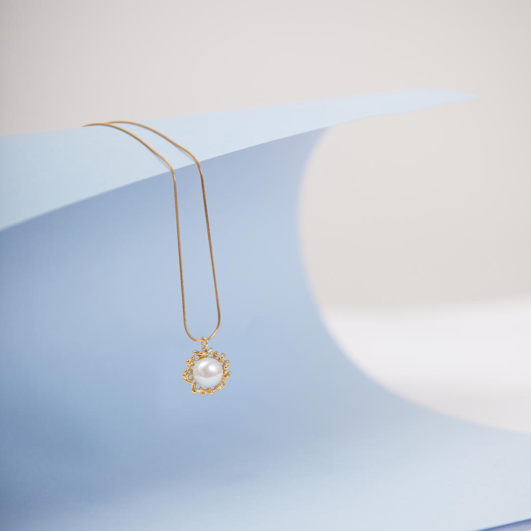 A gold-toned pearl necklace with a lobster closure, displayed on a blue textured surface.