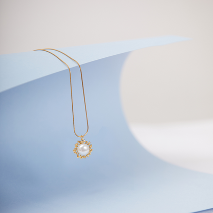 A gold-toned pearl necklace with a lobster closure, displayed on a blue textured surface.