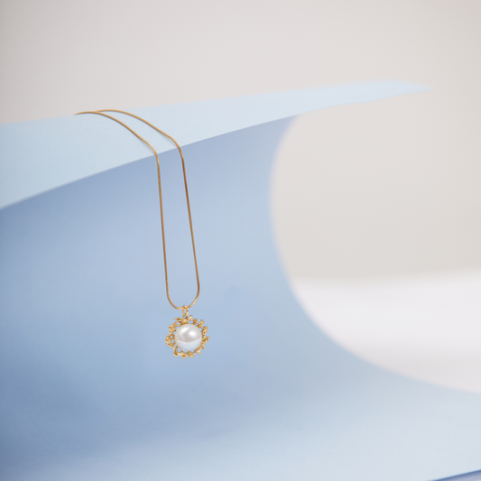 A gold-toned pearl necklace with a lobster closure, displayed on a blue textured surface.
