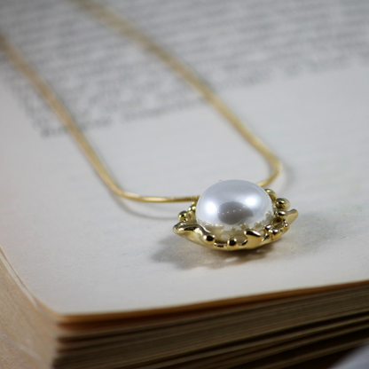 A gold-toned pearl necklace with a lobster closure, displayed on a book