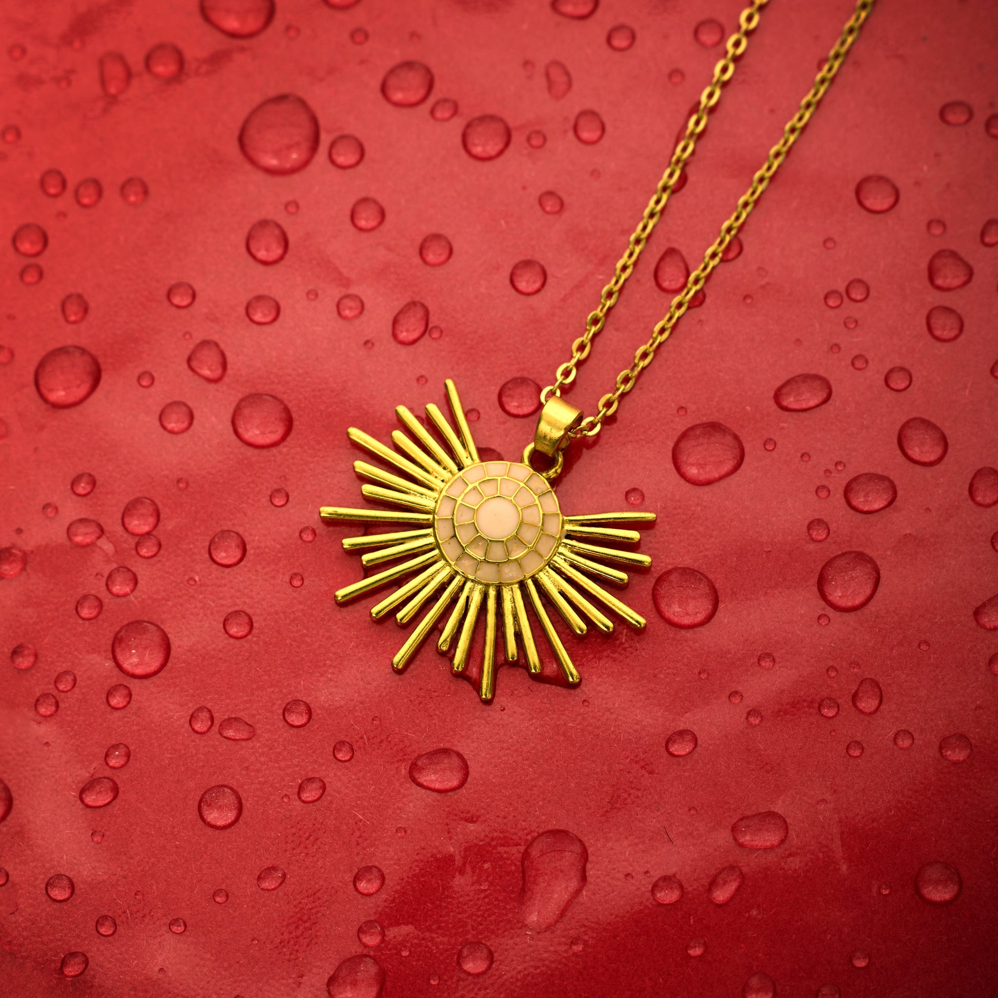 gold-plated necklace with a half sun enamel pendant, held up against a red background.