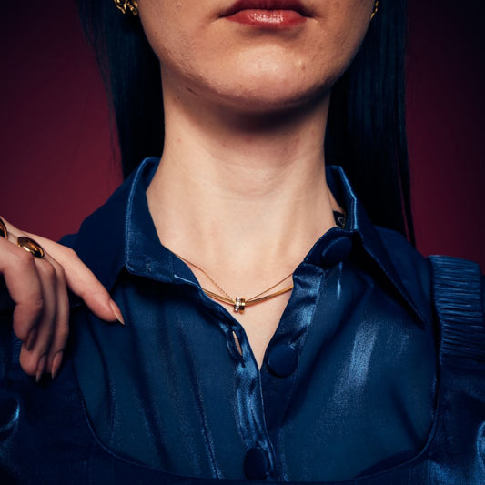 A person wearing a blue shirt and a gold-colored necklace with a shimmering pendant.